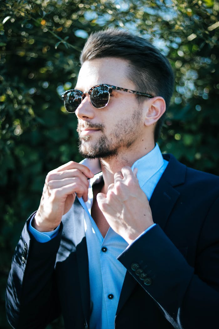 Mastering the First Impression: Your intriguing post title goes here Fashionable man adjusting his suit and sunglasses outdoors on a sunny day.