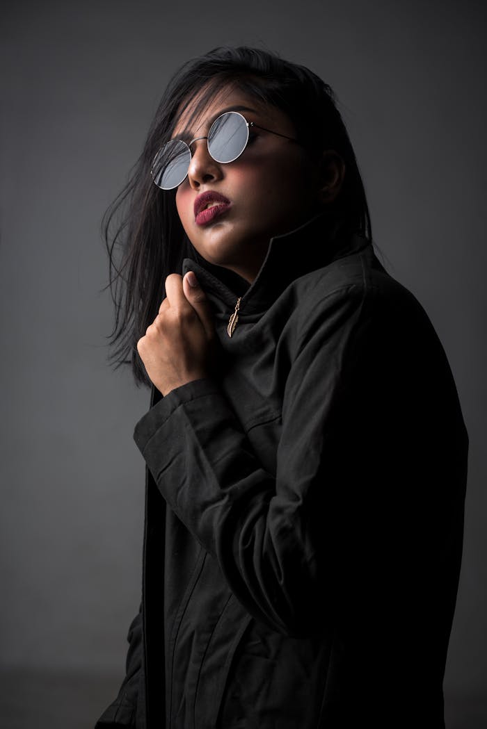 The Art of Drawing Readers In: Your attractive post title goes here Stylish portrait of a woman posing in a studio with dark fashion attire and round sunglasses.